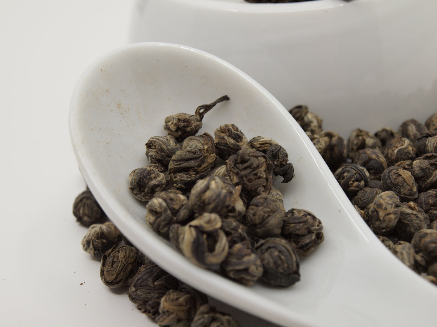 jasmine pearl tea in a white porcelain spoon, ultra close up