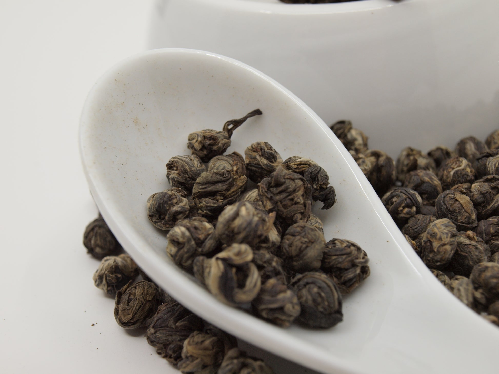 jasmine pearl tea in a white porcelain spoon, ultra close up
